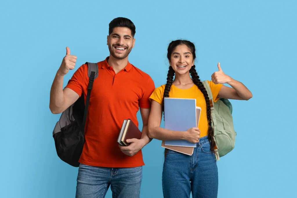 Happy students holding books and giving thumbs up for Study in Europe with Edge Overseas educational consultancy